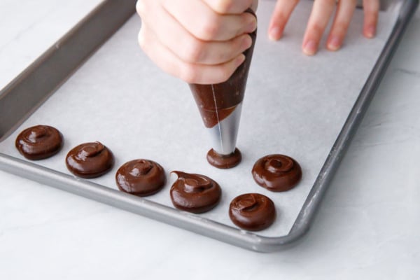 Piping dollops of ganache onto parchment for the cookie centers