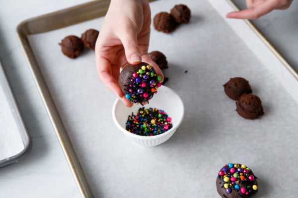Dipping the tops of shaped cookie dough balls in colorful rainbow sprinkles