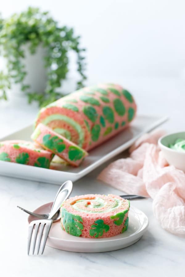 Slice of pink & green Monstera Cake Roll on white with houseplant in the background