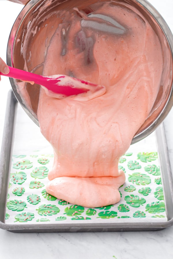 Pouring the pink cake batter base into the jelly roll pan on top of the stenciled design