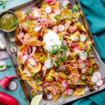 Overhead, sheet pan of Loaded Smoked Chicken Nachos with radishes, micro cilantro on a turquoise background