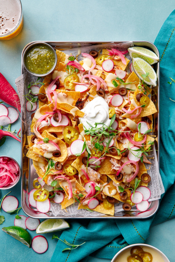 Overhead, sheet pan of Loaded Smoked Chicken Nachos with radishes, micro cilantro on a turquoise background