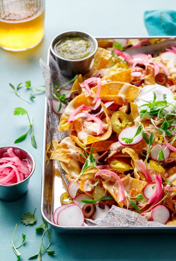 Pan of Loaded Smoked Chicken Nachos with small dishes of salsa verde and pickled red onion, glass of beer