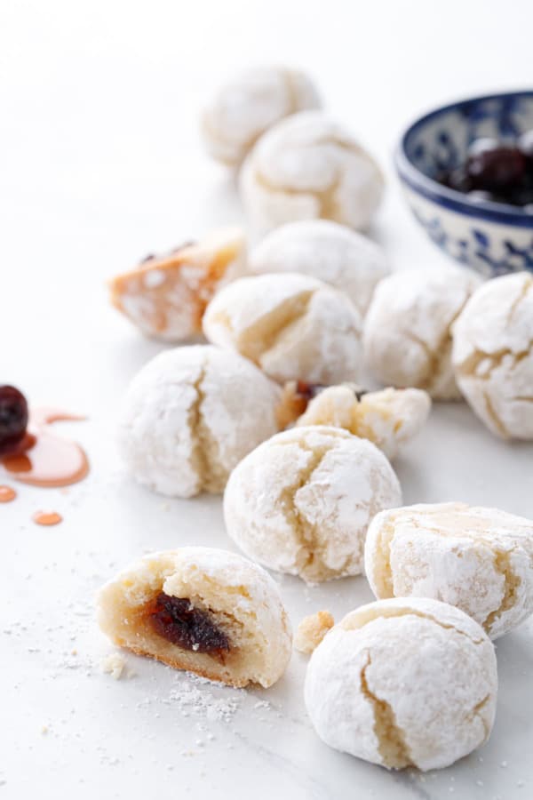 Scattered cookies on a white background, one cut in half to show the cherry filling.