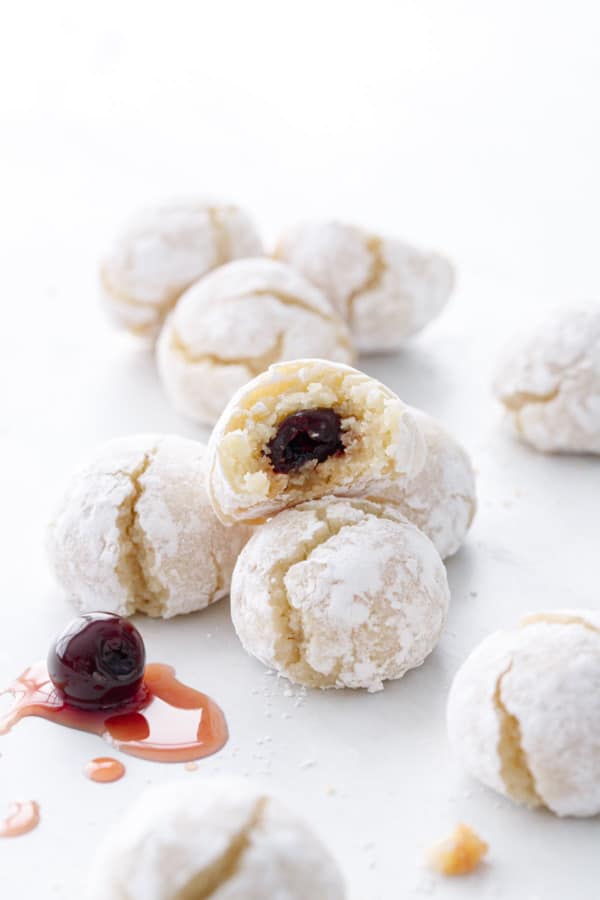 Scattered cookies on a white background, one cut in half to show the cherry filling.