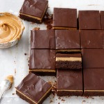 Sliced peanut butter ganache brownies on parchment, bowl of peanut butter on the side