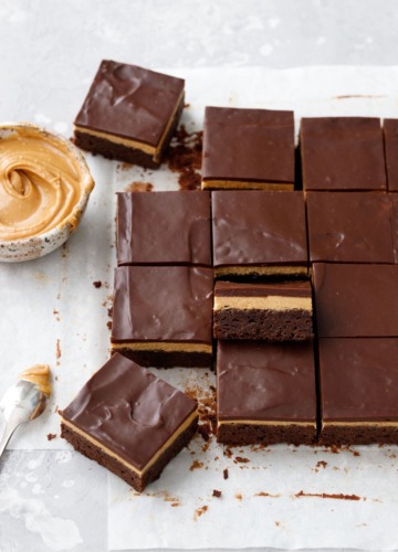 Sliced peanut butter ganache brownies on parchment, bowl of peanut butter on the side