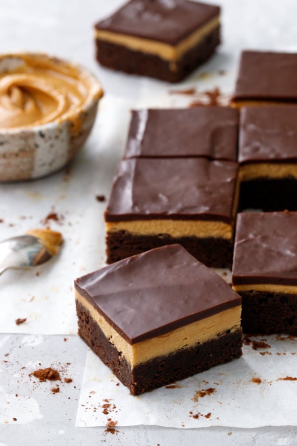 Squares of Milk Chocolate Peanut Butter Ganache Brownies on parchment, gray background, bowl of peanut butter