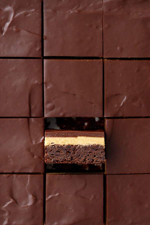 Overheat, sliced squares of Milk Chocolate Peanut Butter Ganache Brownies, one brownie tilted on its side to show the layers