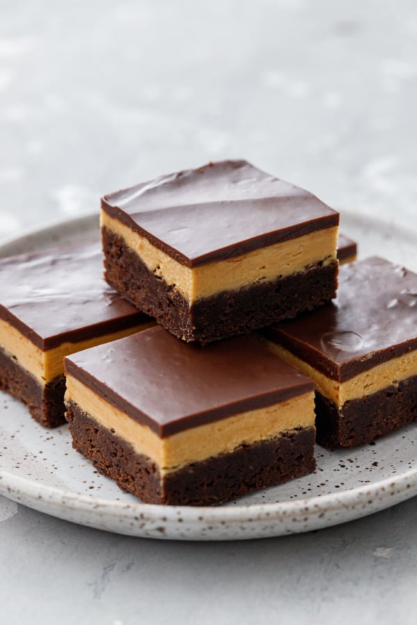 Plate with 5 neat squares of Milk Chocolate Peanut Butter Ganache Brownies, cleanly cut to show the 3 distinct layers