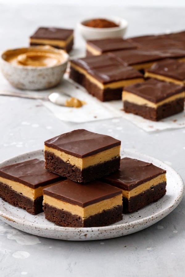 Plate of Milk Chocolate Peanut Butter Ganache Brownies, more in the background with bowl of peanut butter