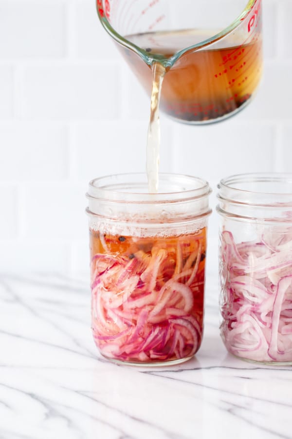 Sliced onions in glass mason jars, pouring the hot vinegar brine over top.