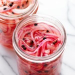 Two jars of pickled red onions in glass jars on a marble background