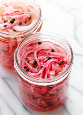 Two jars of pickled red onions in glass jars on a marble background