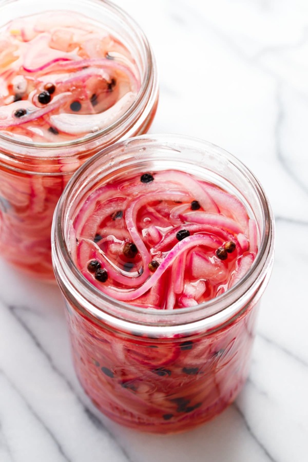 Two jars of pickled red onions in glass jars on a marble background