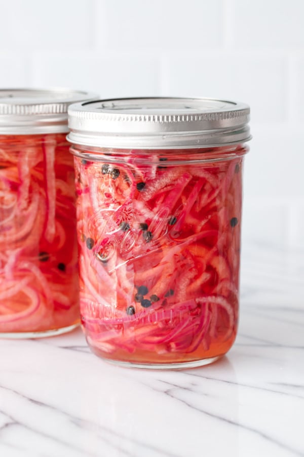Two lidded glass mason jars filled with Quick Pickled Red Onions