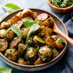 Shallow bowl filled with roasted potatoes tossed with arugula chimichurri, small baby arugula leaves scattered on top