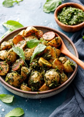 Shallow bowl filled with roasted potatoes tossed with arugula chimichurri, small baby arugula leaves scattered on top