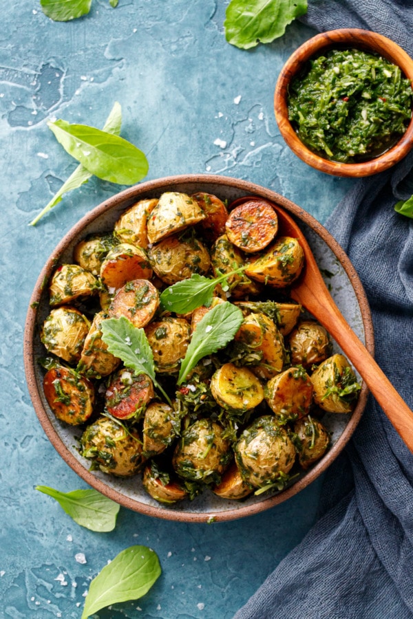 Ceramic bowl with halved baby potatoes, roasted until golden and tossed with arugula chimichurri sauce, small bowl on the side