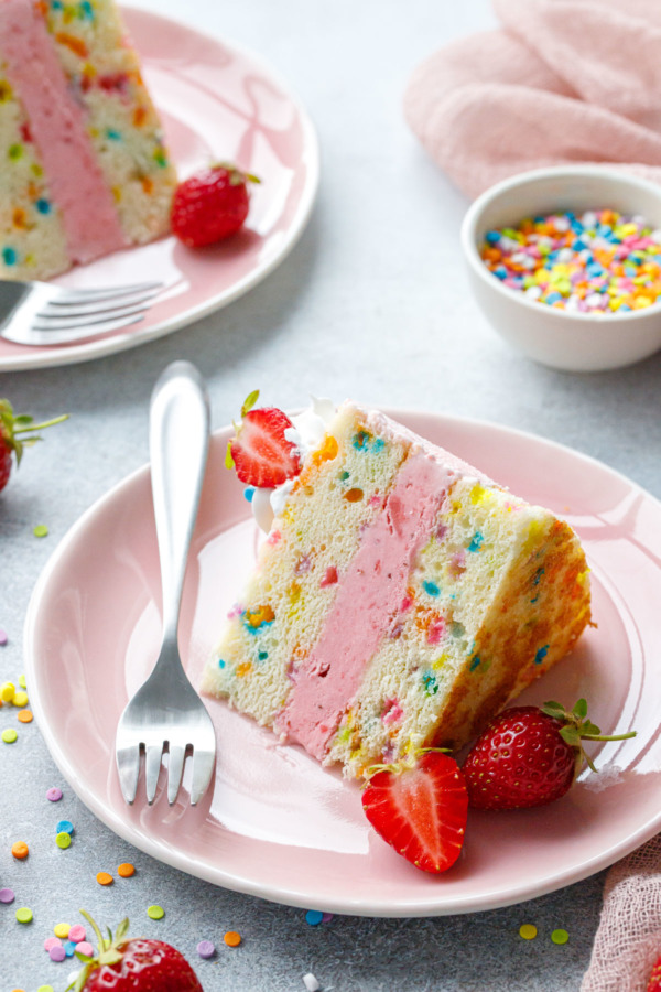 Slice of Strawberry Funfetti Ice Cream Cake on a pink plate with forks and berries