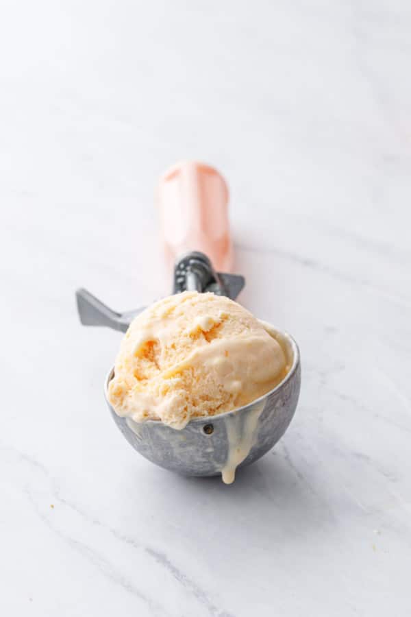Pink handled vintage ice cream scoop with dripping peach ice cream