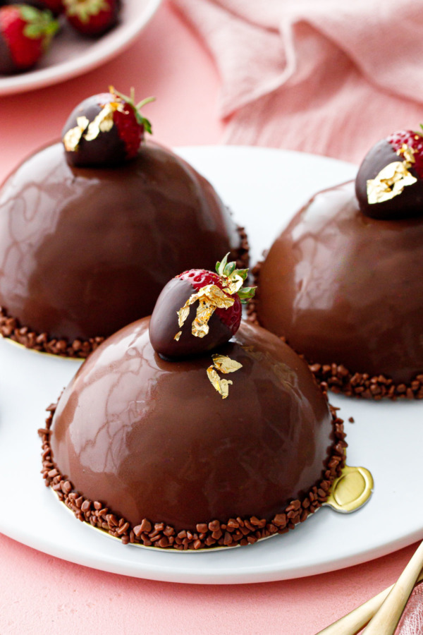 Ganache-glazed domes of strawberry mousse, topped with mini chocolate dipped strawberries and gold leaf