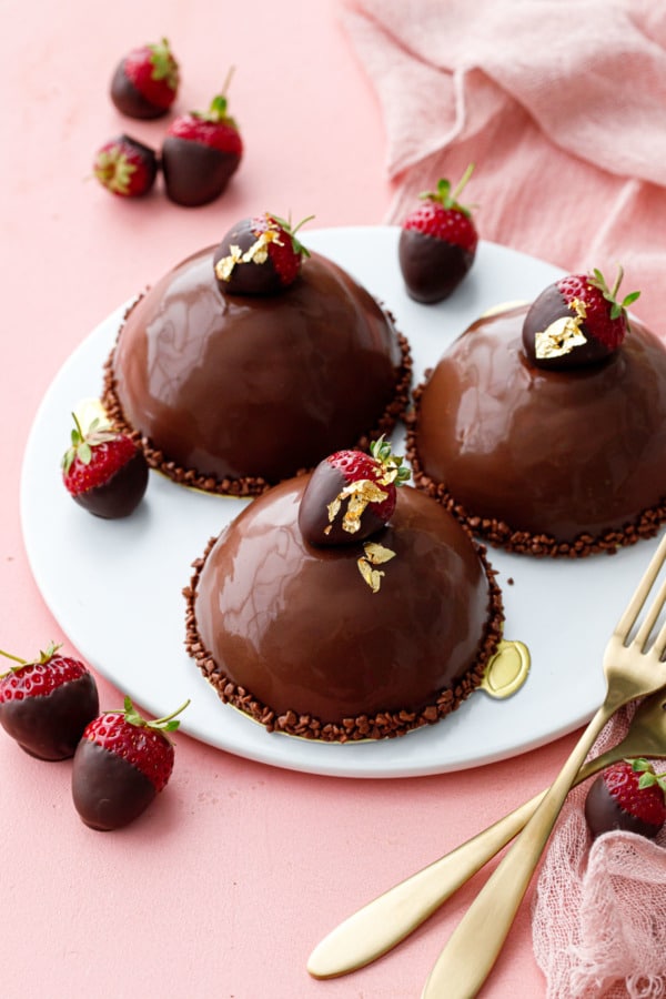 Three domes covered in ganache, on a white plate, pink background