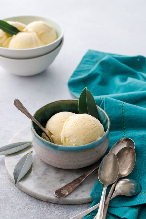 Scoops of bay leaf ice cream in two bowls, with vintage spoons and fresh bay leaves