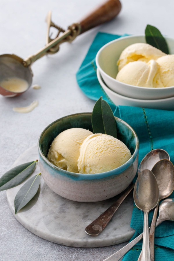 Two bowls of bay leaf ice cream on a gray background, with vintage spoons and ice cream scoop