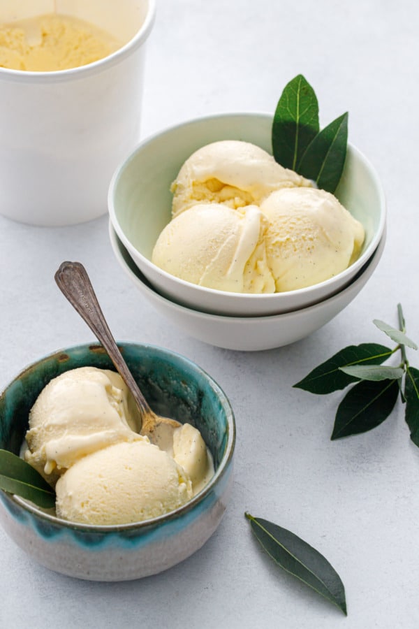 Bowls and ice cream container with scoops of fresh bay leaf and vanilla bean ice cream, fresh bay leaf garnish