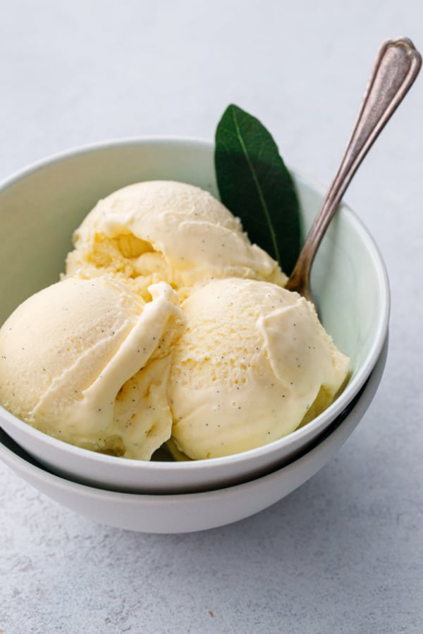 Mint green ceramic bowl with three scoops of homemade ice cream, garnished with a fresh bay leaf