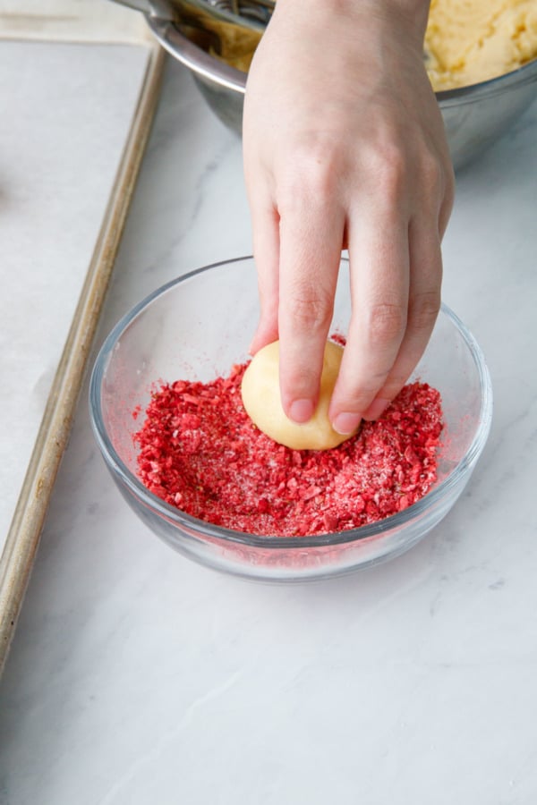 Dipping the tops of the cookie dough balls into ground up freeze-dried strawberries