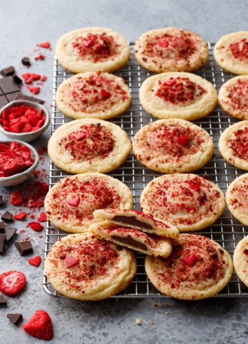 Chocolate Stuffed Strawberry Sugar Cookies on a wire rack, raw chocolate and freeze dried strawberries scattered on the side