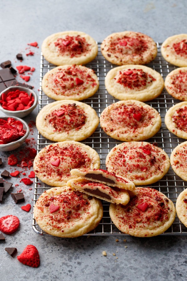 Chocolate Stuffed Strawberry Sugar Cookies on a wire rack, raw chocolate and freeze dried strawberries scattered on the side