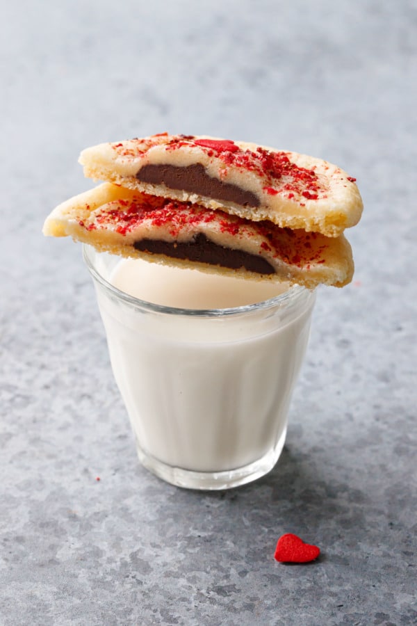 One chocolate-stuffed cookie cut in half, balanced on top of a small glass of milk on a gray background