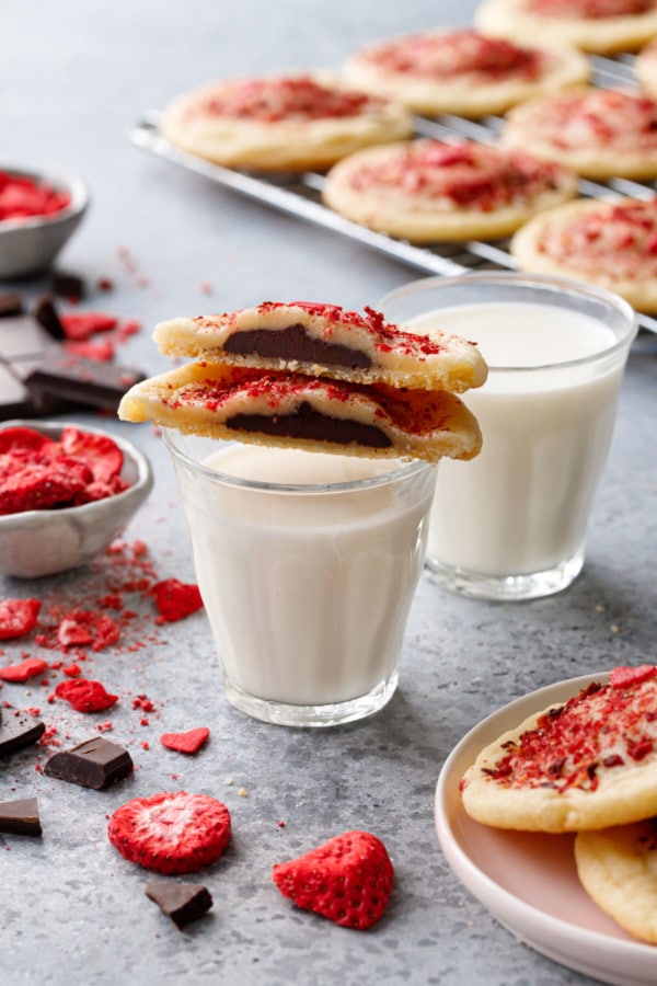 Cookie balanced on a glass of milk, more cookies in the fore/backgrounds with some raw ingredients scattered around