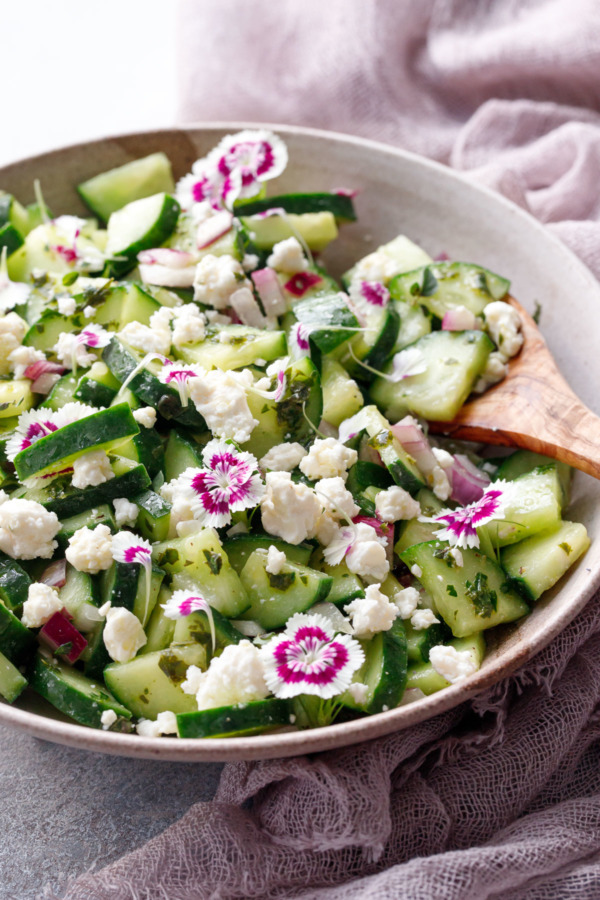 Cucumber & Feta Salad with Herb Vinaigrette and garnished with edible flowers, in bowl with wooden spoon