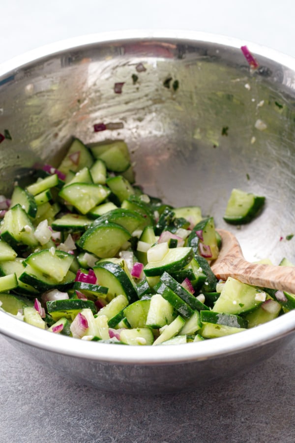 Metal prep bowl with cucumber salad after tossing with herb vinaigrette dressing
