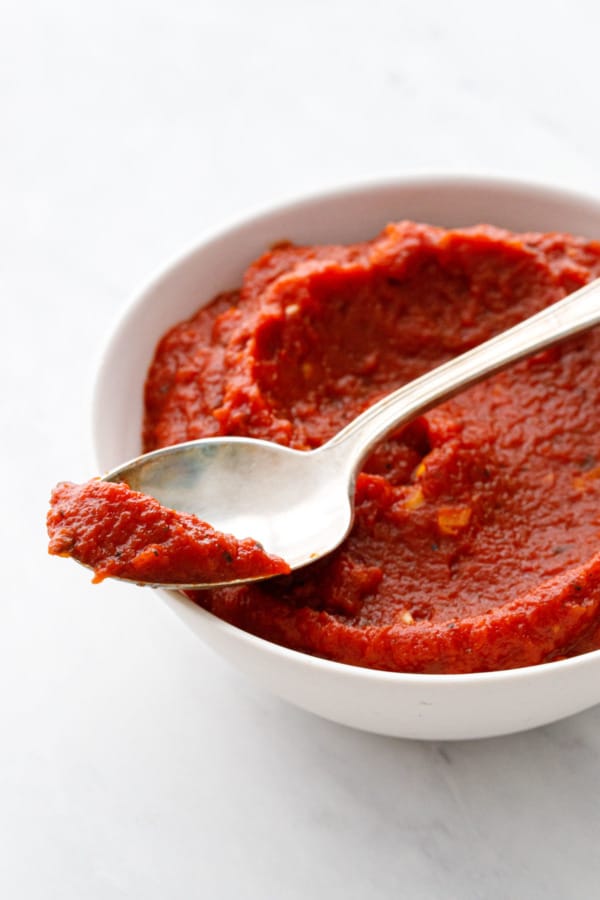 Closeup of a bowl with a spoonful of homemade pizza sauce, zoomed in to show the extra-thick texture