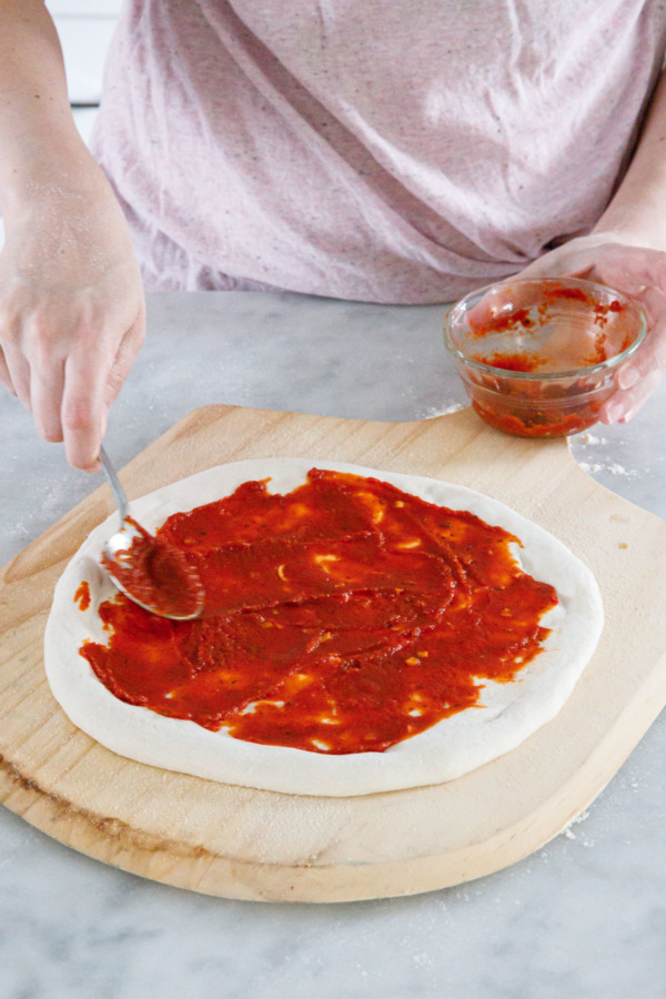 Spreading homemade pizza sauce onto shaped pizza dough with a spoon