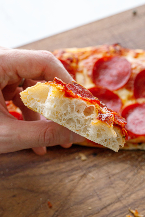 Partially eaten piece of pizza held to show the airy, bubbly texture of the inside crust.