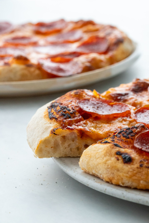 Side view, pepperoni pizza with one slice cut out to show the texture of the crust.