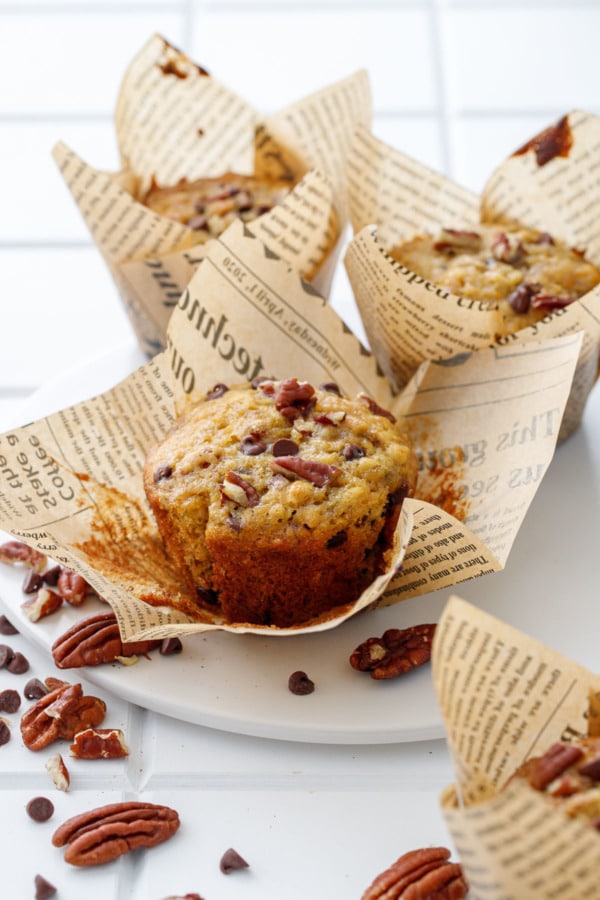 White plate with three banana bread muffins, one wrapper peeled off to show the browned edges of the muffin