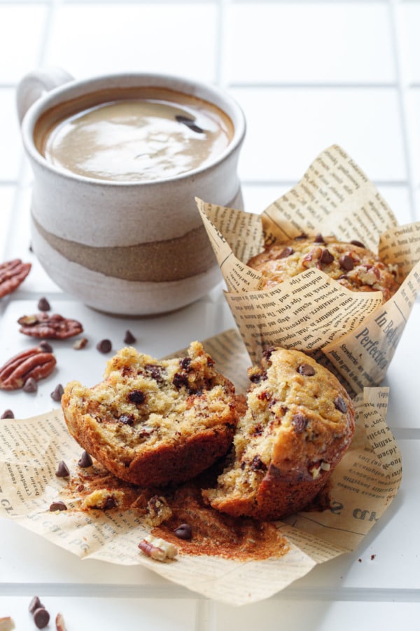 Chocolate chip banana bread muffins, one split in half to show texture, with a cup of coffee in homemade ceramic mug