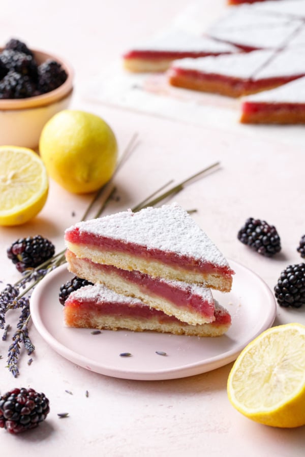 Stack of three triangle shaped Blackberry Lavender Lemon Bars on a pink plate