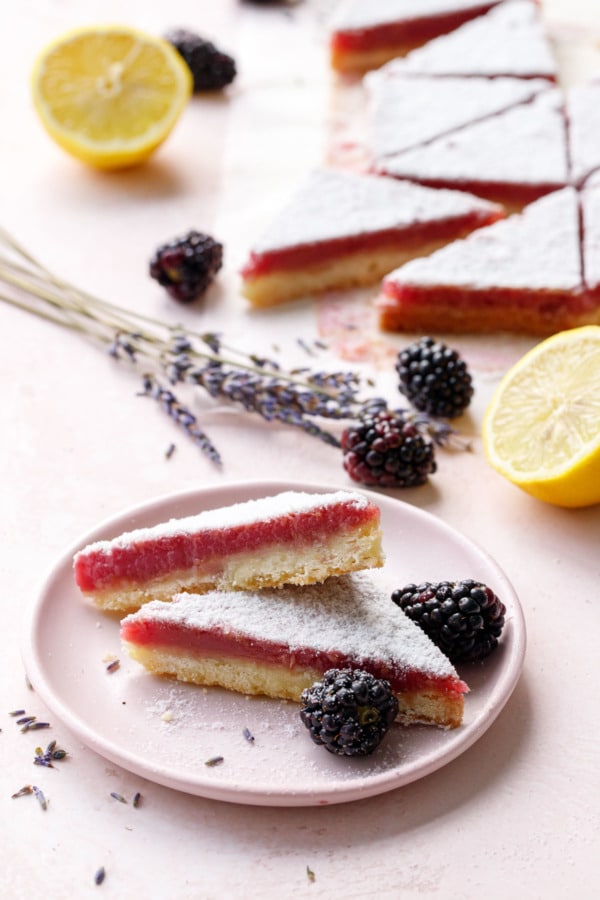 Stack of three Blackberry Lavender Lemon Bars cut into triangles on a pink plate