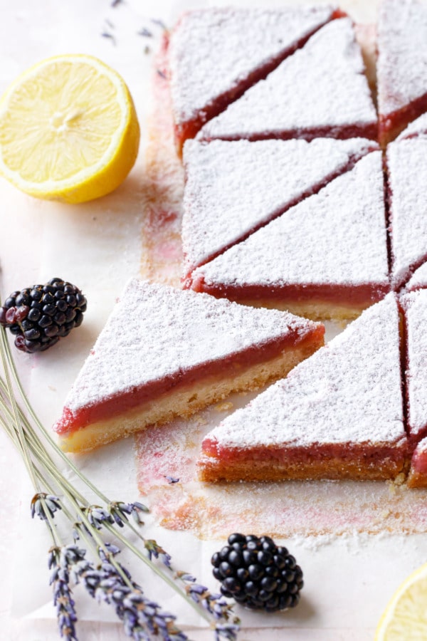 Blackberry Lavender Lemon Bars cut into triangles, defined layers of yellow shortbread and pink topping with powdered sugar