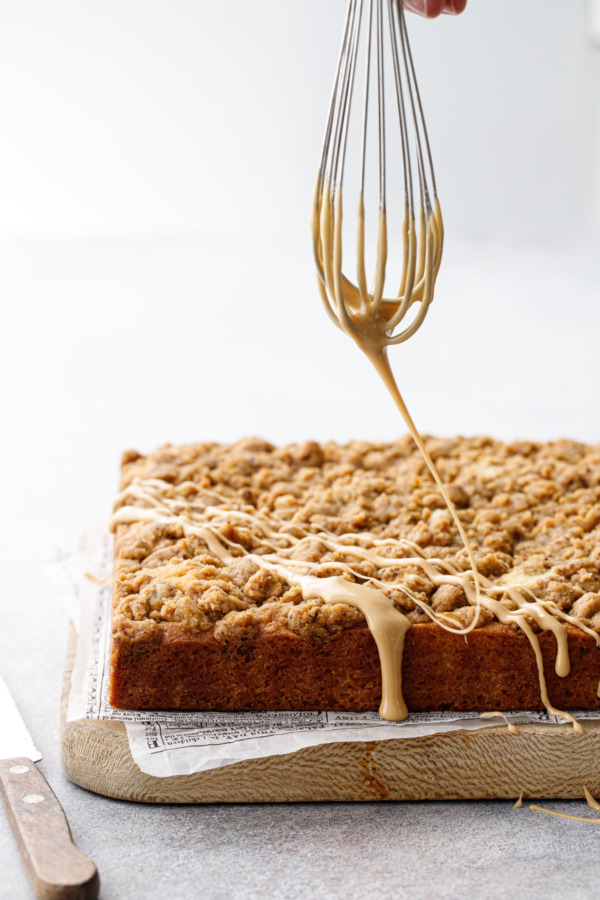 Action shot of whisk drizzling espresso glaze on top of crumb coffee cake.