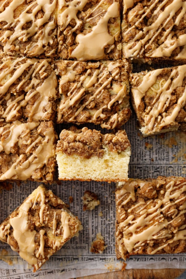 Overhead, grid of cut squares of coffee cake, one on its side to show the cake and crumb layers