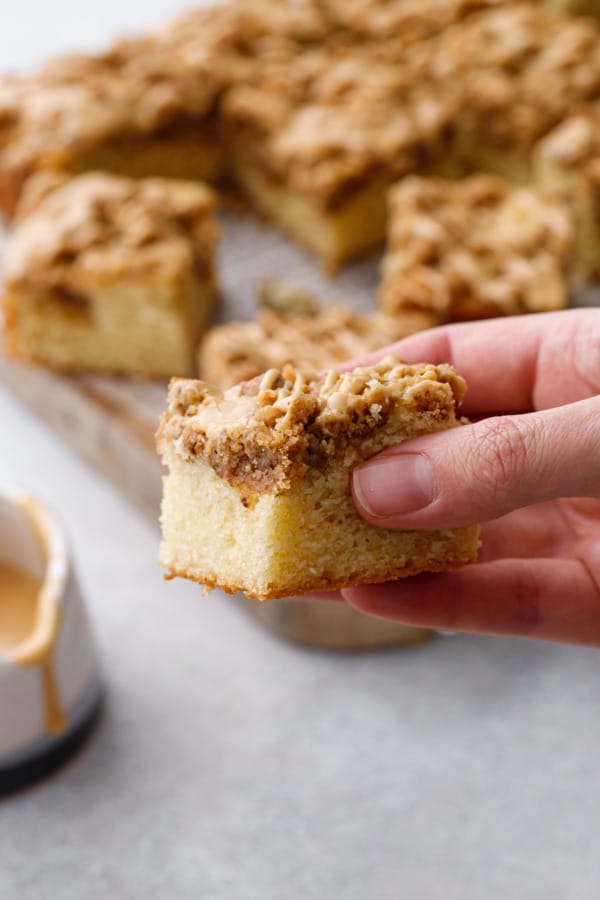 Hand holding a slice of Espresso Crumb Coffee Cake, cutting board with more pieces in the background